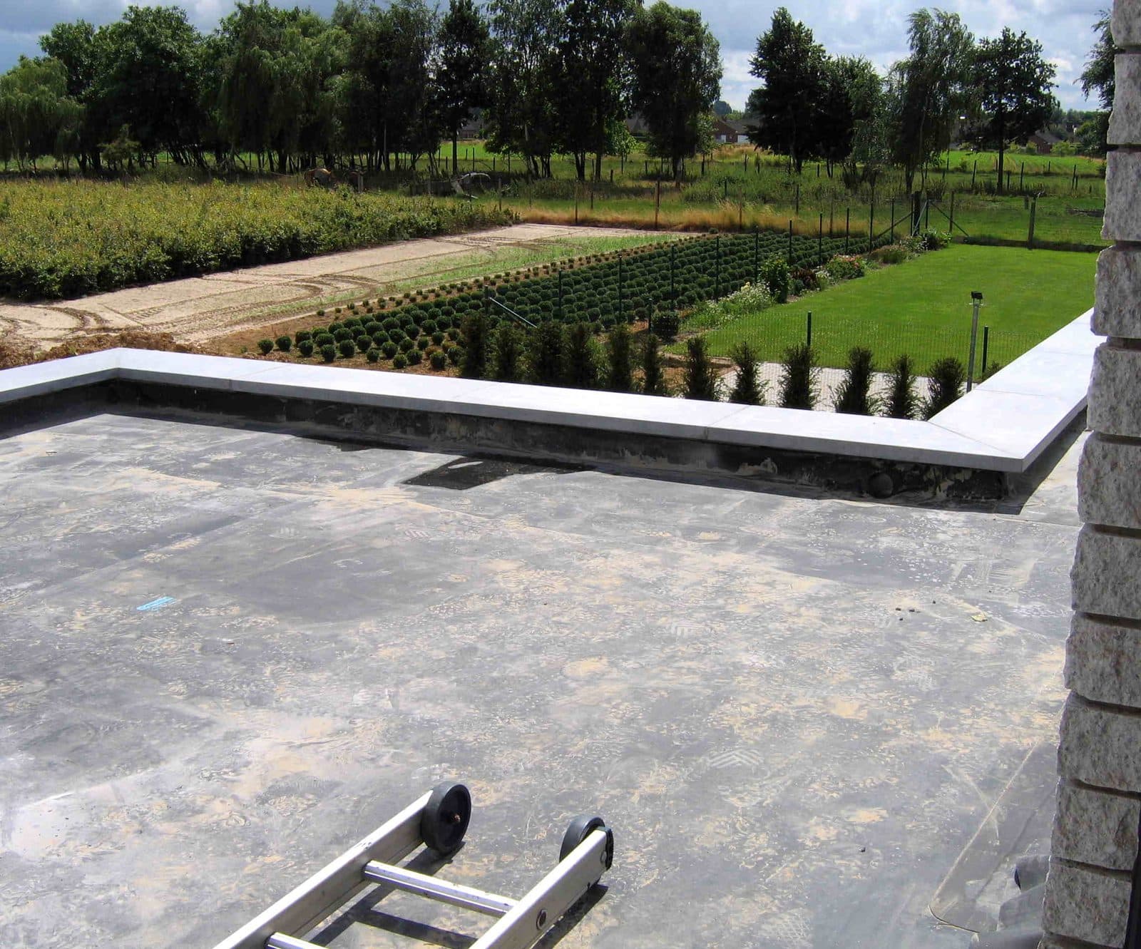 A finished EPDM rubber flat roof with stone coping around the edge and a ladder on the membrane