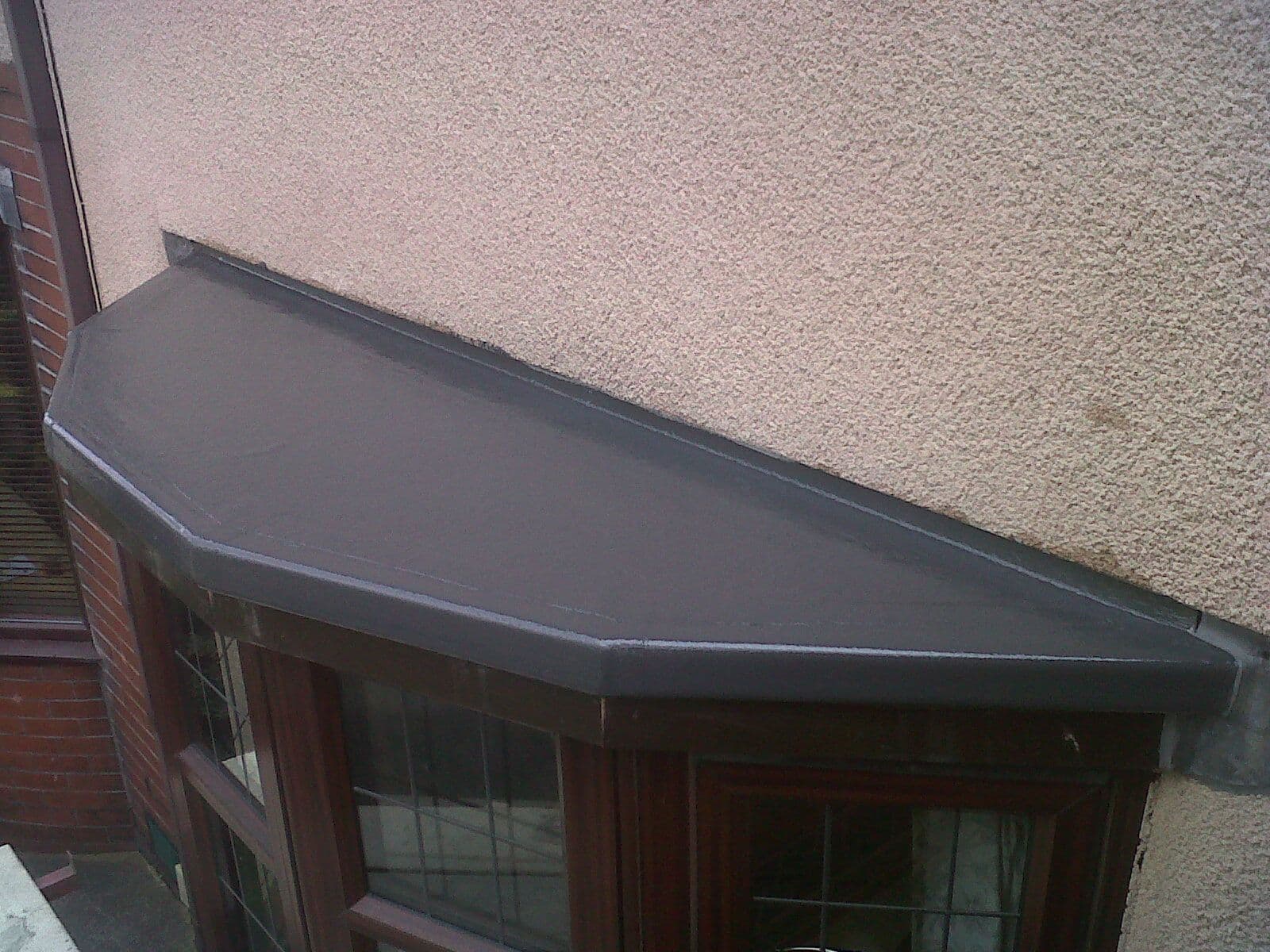 Grey GRP fibreglass roof over a bay window on a stone house