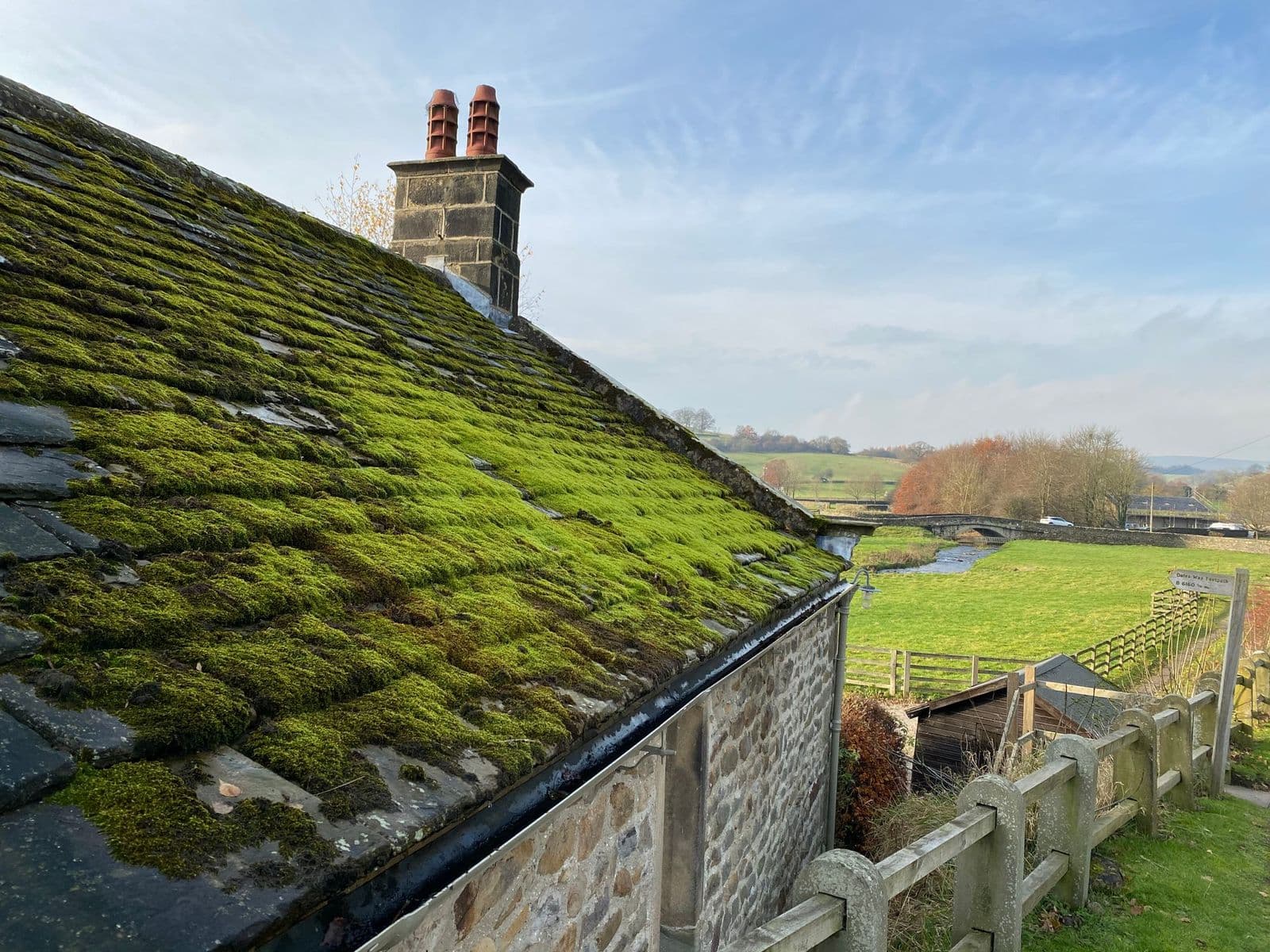 Thick green moss covering the roof of a stone cottage with a chimney