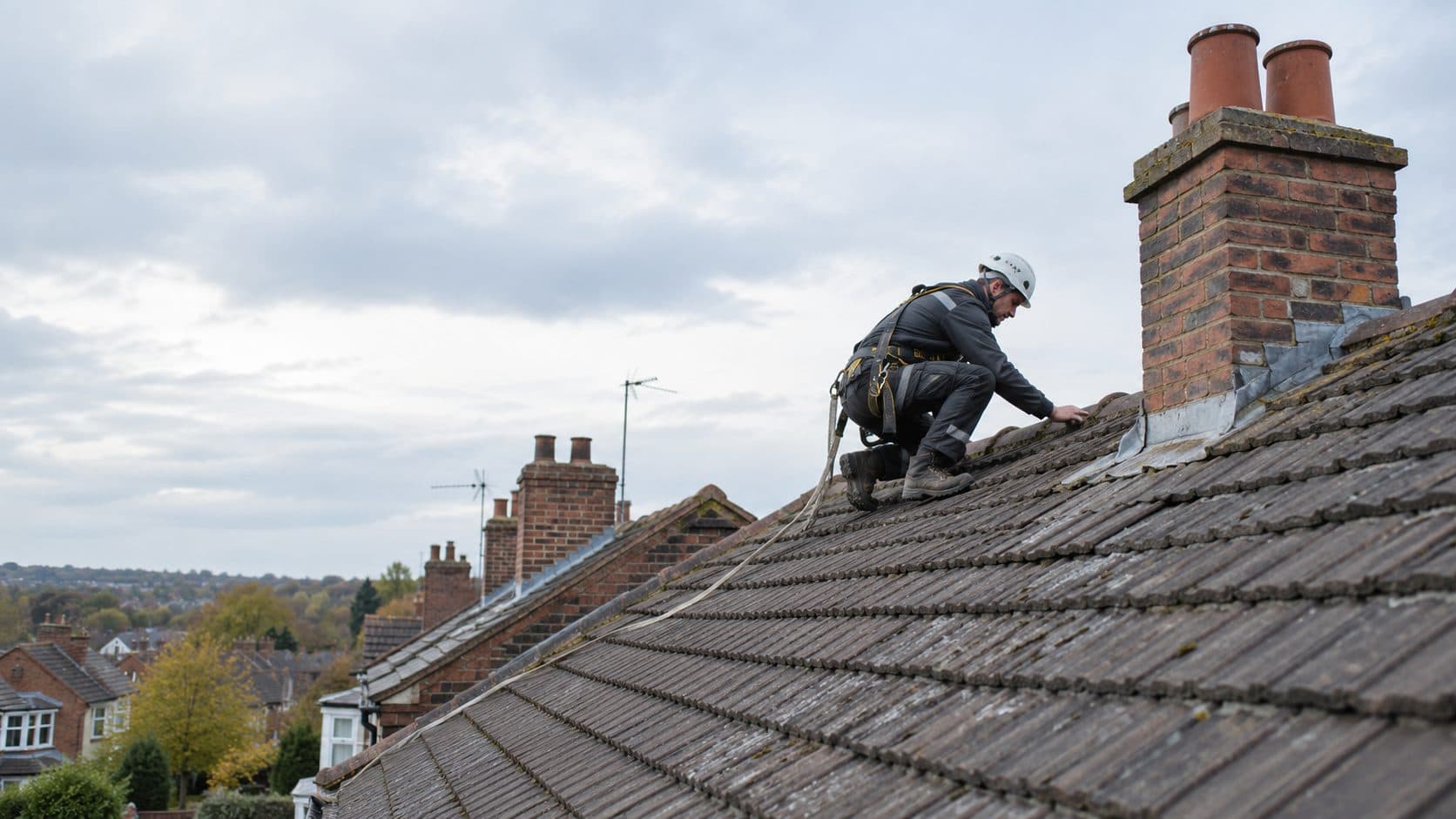 Roofer working at the base of a brick chimney stack on a tiled roof